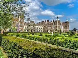Château d'architecture jacobéenne et de style Tudor en briques rouges. Devant le château se trouve un jardin bien entretenu.