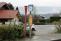 Photographie en couleurs de poteaux Lihsa et J’yBus marquant un arrêt de bus en zone urbaine à Hauteville-sur-Fier.