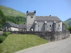 Photographie d'une église en pierre, couverte d'un toit d'ardoises, avec un cimetière en premier plan.