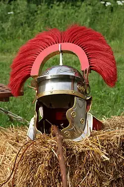 Reconstitution d'un casque Impérial-Gaulois muni d'un couvre-nuque et de paragnathides rivetés. Les oreilles sont dégagées grâce à une ample échancrure latérale qui permet au combattant d'entendre les ordres de l'officier. Les paragnathides épousent la forme de la mâchoire et présentent deux excroissances au niveau du nez et du menton.