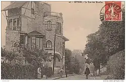 Carte postale en noir et blanc avec un timbre montrant une maison en bordure de route avec un personnage