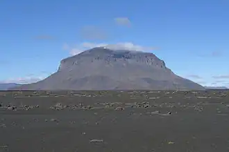 Volcan ayant une forme de chapiteau avec une plaine caillouteuse au premier plan.