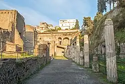 allée avec un bâtiment à gauche, des colonnes à droite et au fond, étage en arcades