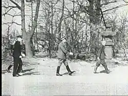 Photo noir et blanc de trois hommes déambulant dans les ruines d'une rue.