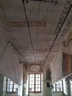 Vue sur un escalier donnant sur une fenêtre où se situe un miroir qui projette un reflet sur l'horloge solaire peinte sur les murs de l'escalier.