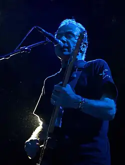 un homme qui joue de la guitare devant un micro dans la nuit.