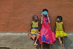 Une jeune fille, souriante, regarde à travers un foldscope. Deux autres enfants rient à côté d'elle.