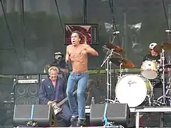 Trois hommes caucasiens sur scène ; le tout premier porte un jean bleu et est torse nu.