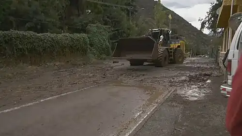 Engin de chantier enlevant la boue accumulée sur une route par une inondation.
