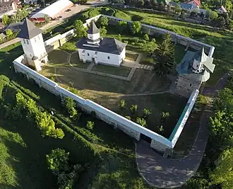 Vue de dessus d'une église et de plusieurs arbres entourés d'un mur rectangulaire. Deux chapelles en forme de tour sont accolées au mur de chaque côté de l'église.