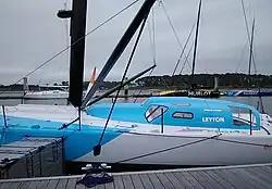 Voilier bleu clair et blanc amarré au ponton. Vue latérale du milieu. Le pont est blanc. La superstructure (rouf et casquette) est bleue.