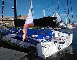 Vue de trois quarts arrière de l'arrière d'un voilier bleu, blanc et jaune amarré au ponton.