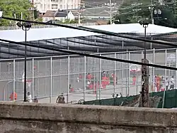 Cour de la prison où se promènent des détenus en vêtements oranges derrière un grillage élevé