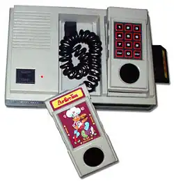 console quadrangulaire grise avec deux manettes en forme de combiné de téléphone. Une cartouche du jeu BurgerTime est posée dessus