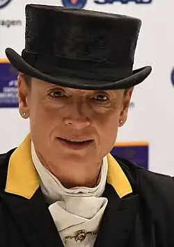 Portait d'une femme avec un chapeau noir et une redingote noire avec le col jaune et une cravate blanche.