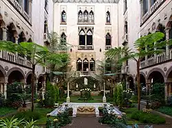 Photo d'une cour intérieure carrée, parsemée d'arbres fins, de fleurs et comportant un parvis central blanc, entouré de quelques sculptures.