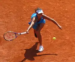 Sur un terrain en terre battue, une joueuse de tennis en bout de course tendant sa raquette pour essayer d'attraper la balle.