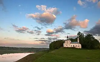 Photographie prise à la tombée de la nuit montrant une église à droite dominant un paysage avec un lac en bas à gauche.