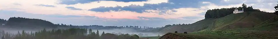 Vallée avec de la brume dominée par des collines, avec à droite l'église.
