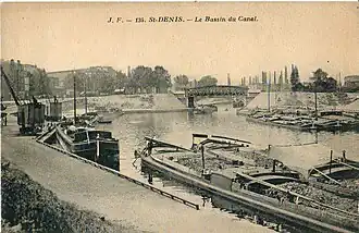 Le canal Saint-Denis, ouvert dès 1821, est la première infrastructure de transport performante qui irrigua la Plaine, à une époque où les transports par route étaient coûteux et lents. On voit ici le bassin de la Maltournée, avec des péniches déchargeant du charbon, sans doute destiné à l'usine à gaz du Cornillon.
