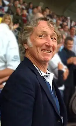 Photo en buste d'un homme en costume bleu se tenant de trois-quart dans une tribune de stade