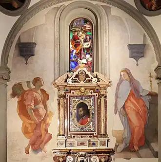 Fresque. L'ange et Marie se dressent de part et d'autre d'un monument commémoratif comprenant le portrait d'un homme.