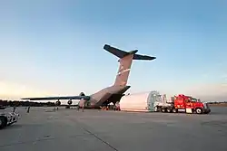 Chargement par la porte arrière, dont l'ouverture est spécifique. Le satellite est contenu dans une structure blanche.