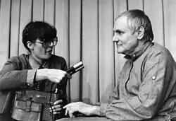 Photo en niveaux de gris d'un homme à gauche à qui une femme tend un micro.