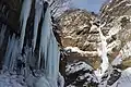 Photo couleur d'une chute d'eau gelée, le long d'une paroi rocheuse enneigée.