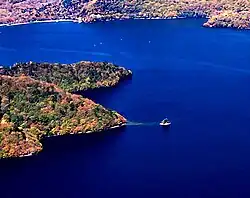 Photo couleur d'un îlot dans une étendue d'eau couleur bleu de cobalt. La rive boisée du lac en arrière-plan.
