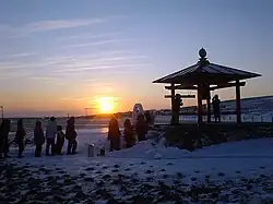 Photo couleur d'un lever de soleil vu du bord d'une plage enneigée.