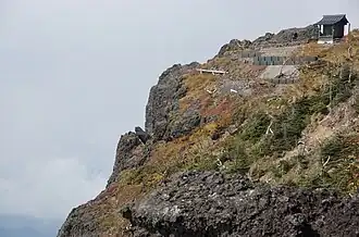 Photo couleur d'un petit sanctuaire en bois au sommet d'une montagne sous une ciel nuageux.
