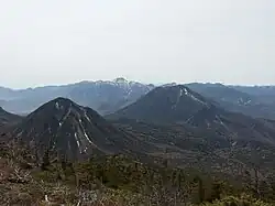 Photo couleur de deux montagnes, avec, en arrière-plan, une chaîne de montagnes sous un ciel nuageux.