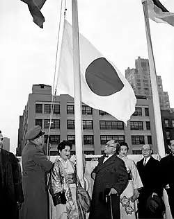 Un groupe d'hommes et femmes regardant un drapeau se faisant hisser.