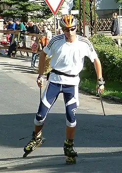 Portrait de Jason Lamy-Chappuis sur des rollers, portant un casque orange, des lunettes, un maillot blanc et un pantalon bleu.