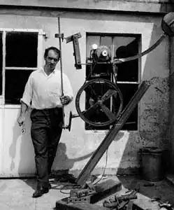 L'assemblage : Jean Tinguely devant son atelier avec un assemblage en cours. 1963.