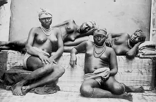 Photographie de quatre femmes dénudées, portant une coiffe, allongées ou assises autour d'une paillasse.