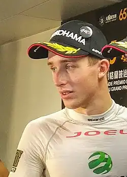 Photographie en plan poitrine d'un homme blanc, vu de trois-quarts gauche, habillé en blanc, casquette noire sur la tête.