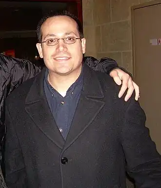 Homme caucasien portant des lunettes, une chemise bleue foncée, et un manteau noir (photo prise en 2007).