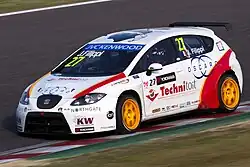 Voiture blanche vue de trois-quarts, sur des vibreurs rouges et blancs, à gauche de la piste.