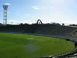 Stade de football avec une pelouse verte sans aucun joueur, sous un ciel bleu.