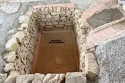 Trou rectangulaire dans le sol servant d'espace de stockage relié à des canalisations en briques sur la droite