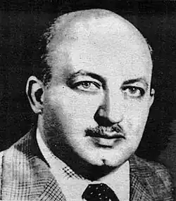 portrait noir et blanc de face d'un homme moustachu chauve aux yeux clairs.