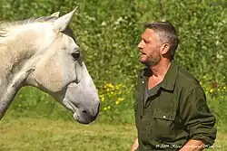 Photographie de la tête d'un cheval gris et du buste d'un homme, les deux s'entre-regardant.