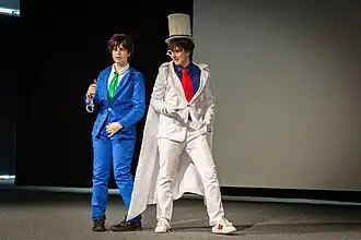 photo de 2 personnages (un en costume blanc et l'autre en costume bleue) sur scène