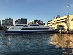 Photographie en couleurs, représentant un bateau et des bâtiments.