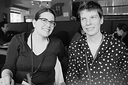 Photo noir et blanc de deux jeunes femmes assises côte à côte, portant un cordon de session, l'une d'elle porte des lunettes