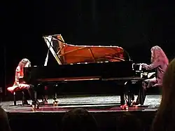 Photographie couleurs de 2 pianistes blanchesjouant face à face sur leur piano à queue