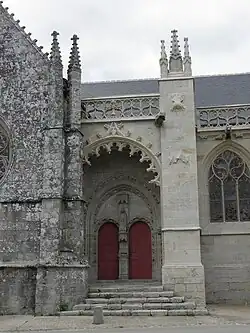 Vue depuis l'extérieur, de face. Au fond du porche, un portail à deux portes. Entre les deux portes, un bénitier surmonté d'une statue.