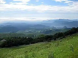 Photo couleur montrant des plaines et des collines verdoyantes à perte de vue sous un ciel bleu nuageux.